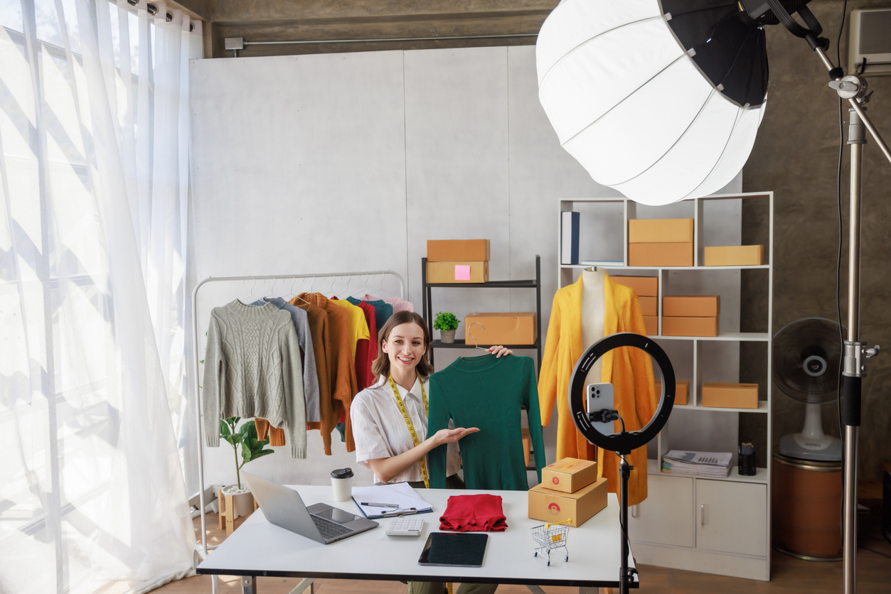 concept of selling streaming online,blogger or seller woman showing clothes in front of smartphone camera for business purpose online recording vlog video live chat and selling at her chanel in studio